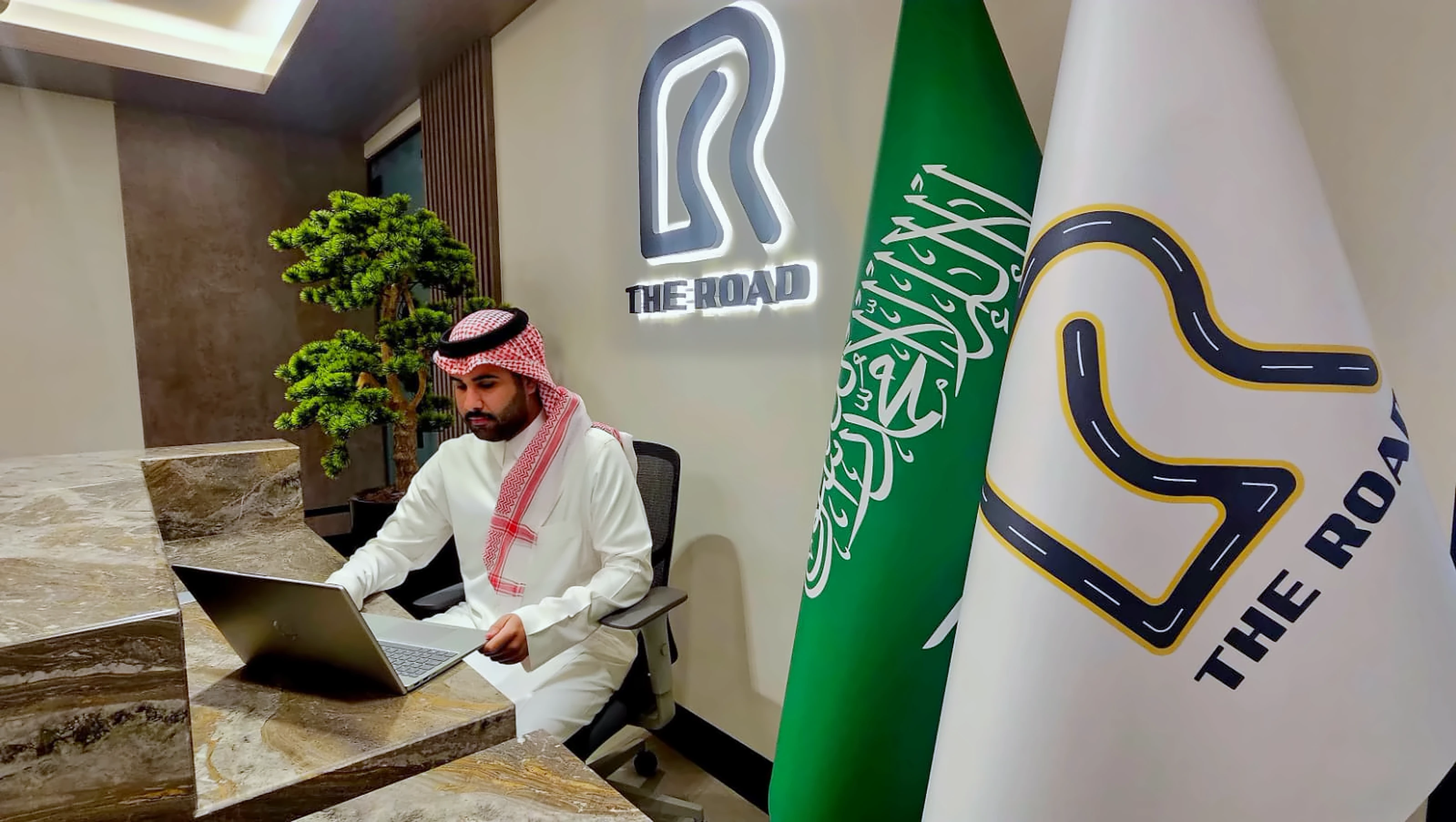A colleague at the reception desk in The Road head office, below the illuminated logo